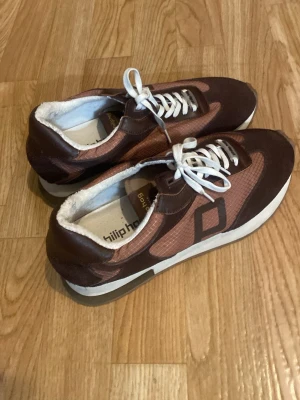 Bruna sneakers från Philip Hog - Snygga sneakers från Philip Hog i brunt och kopparfärgat tyg med detaljer i mocka och vita skosnören. Skorna har en klassisk låg modell och vit sula. Perfekta för dig som gillar en retroinspirerad stil med moderna material och coola färgkombinationer. Priset kan diskuteras vid snabb affär!