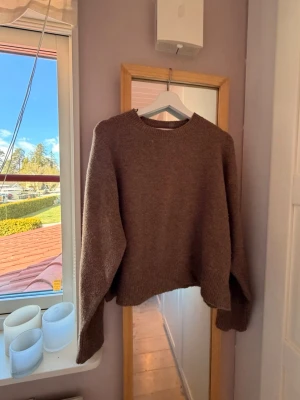Brun oversized stickad tröja - Mysig brun stickad tröja med oversized passform och rund halsringning. Tröjan har långa ärmar och ribbstickade muddar vid ärmslut och nederkant. Perfekt för lager-på-lager och en avslappnad stil.