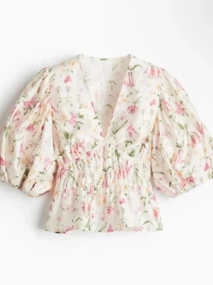 Blommig blus med puffärm och v-ringning - Söt blommig blus i vitt med rosa och gröna blommor, djup v-ringning och bred resår i midjan. Blusen har puffiga trekvartsärmar och är tillverkad i ett lätt, luftigt tyg som ger en romantisk känsla.
