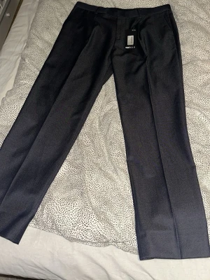 Två par kostymbyxor i olika färger - Säljer två par kostymbyxor, ett par i mörkgrått med klassisk rak passform och ett par i ljusbrunt med avslappnad look. Perfekta för en stilren och modern outfit. Båda har pressveck och midjeresår för extra komfort.