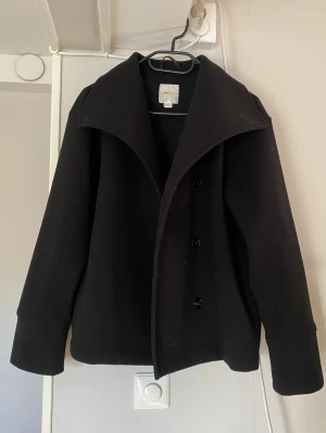 Kappa - Stilren svart kappa med bred krage och tre knappar framtill. Klassisk rak passform och långa ärmar. Perfekt för dig som gillar en tidlös look. Från Gina Tricot Young
