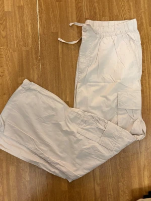 Beiga cargobyxor - jack jones - Säljer ett par beiga cargobyxor med elastisk midja och dragsko. Byxorna har flera praktiska fickor på sidorna och är tillverkade i ett lätt och bekvämt material. Perfekta för en avslappnad och trendig stil.