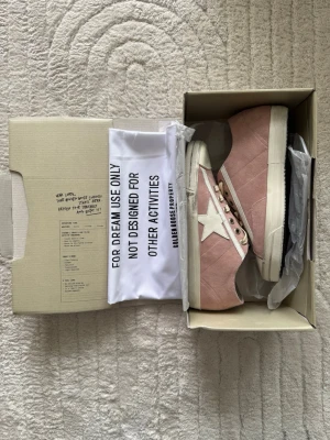  Golden Goose sneakers med stjärna (Cream/42) - Snygga rosa sneakers från Golden Goose med vit stjärndetalj på sidan och vita snören. Skorna har en klassisk låg siluett och vit sula med svart rand. Materialet är canvas och detaljer i läder. Perfekta för dig som gillar streetstyle och vill sticka ut.