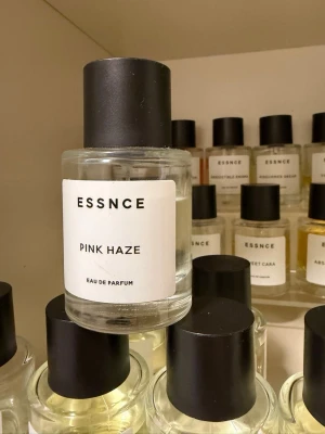 ESSNCE Pink Haze Eau de Parfum - ESSNCE Pink Haze Eau de Parfum kommer i en stilren, rund glasflaska med svart lock och minimalistisk vit etikett. Doften är modern och flaskan är lätt att ta med i väskan. Perfekt för dig som gillar enkla och snygga parfymflaskor.