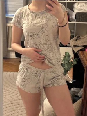 Sööötaste Disney pyjamasset❤️ - Pyjamasset i beige med svarta Disney-figurer tryckta över hela tyget. Setet består av en t-shirt med rund hals och korta ärmar samt shorts med dragsko i midjan. Perfekt för att chilla hemma eller sova bekvämt. Superfina❤️