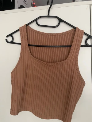 3 toppar  - Säljer 3 crop tops, en i brun nyans med breda axelband, en svart med korsade axelband och en svart med fyrkantig rigning. Alla är tillverkade i stretchigt material och har en tight passform som framhäver figuren. Perfekta för att styla med jeans eller kjol. Alla för 30 kr eller en för 15 kr