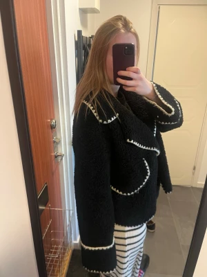 Svart teddyjacka med vita detaljer - Säljer en svart teddyjacka med vita sömmar. Materialet är fluffigt och mjukt, använd en del men fortfarande i bra skick