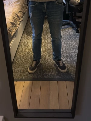 Blå slitna jeans från Replay - Säljer ett par blå jeans från Replay med snygga slitningar och en klassisk femficksmodell. Jeansen har normal passform och är gjorda i mjukt denimtyg som sitter skönt. Perfekta för dig som gillar en avslappnad och trendig stil.