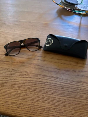 Ray-Ban svarta solglasögon Wayfarer - Snygga svarta Ray-Ban Wayfarer solglasögon med klassisk form och mörka glas. Kommer med original svart fodral i skinn. Perfekta för att lyfta din stil och skydda ögonen mot solen. De är storlek 56