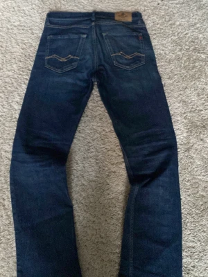 Mörkblå jeans från Replay - Säljer ett par mörkblå jeans från Replay med klassisk femficksdesign och snygga kontrastsömmar på bakfickorna. Jeansen har normal midja och raka ben. Tillverkade i slitstark denim med Replay-lapp bak i midjan.