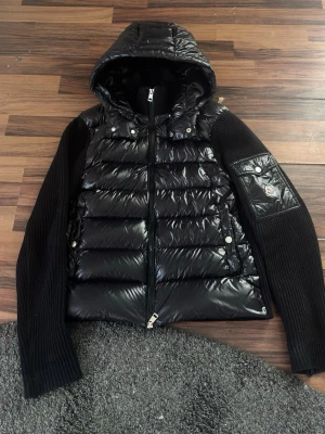 Moncler cardigan  - Säljer en stilren och populär Moncler cardigan i storlek S. Modellen kombinerar blank dunväst framtill med stickade ärmar, vilket gör den både varm och smidig – perfekt som lätt jacka eller lager på lager.  ✔ Äkta Moncler (DISA-certifierad – se bild) ✔ Fint skick överlag ✔ Klassisk svart färg – passar till allt ✔ Bekväm och lätt att bära  Skick: Jackan är i bra skick men dragkedjan har tappat en liten bit längst ner, vilket gör att den kan vara lite känslig när man knäpper den (kan ibland hoppa)