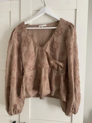 Beige blus  - Beige blus från nakd med blommor. Superfin men ena blomman har gått upp lite som man ser på bild 3, annars bra skick. Inte helt säker men har för mig storlek 36🥰