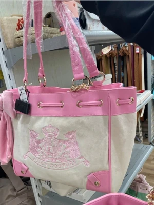 Juicy Couture daydreamer scottie tote rosa och vit  - Snygg handväska från Juicy Couture i ljusrosa och vitt med broderad logga framtill. Väskan har detaljer i rosa konstläder, guldiga metalldelar och långa axelband. Materialet är en mix av mockaimitation och konstläder. Perfekt för dig som gillar en söt och trendig look.