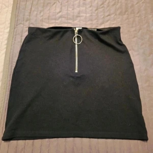 Kjol med dragkedja H&M Divided S - Svart, tight kortkjol med en snygg silverfärgad dragkedja framtill och stor ring som detalj. Kjolen är rak i modellen och tillverkad i ett mjukt bomullstyg med lite stretch. Perfekt för dig som gillar minimalistisk och edgy stil.  Kan även hämtas I Partille  E2