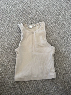 Beige ribbad linnetopp - Säljer en enkel och stilren beige linnetopp med ribbad struktur. Toppen är ärmlös och har en klassisk rund halsringning. Perfekt att matcha med jeans eller kjol för en avslappnad look.