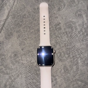 Apple Watch SE 40mm silver med vit sportband - Säljer en Apple Watch SE 40mm i silver med vit sportband. Klockan har en fyrkantig touchskärm och aluminiumboett. Bandet är mjukt och flexibelt, perfekt för dig som gillar stilren och modern design. GPS och pulsmätare ingår.   Batterihälsa : 96%