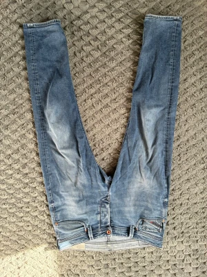 Blå slim fit jeans från diesel - Snygga ljusblå slim fit jeans från diesel med klassisk femficksdesign och diskreta slitningar framtill. Jeansen har en skön stretchig känsla och detaljer som läderpatch bak och orange sömmar vid fickorna. Perfekta för en avslappnad och trendig look.