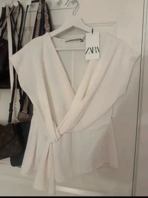 Vit omlottopp från ZARA - Snygg vit omlottopp från ZARA med knyt i midjan och korta ärmar. Helt ny, passar till alla tillfällen