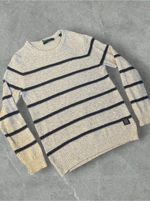 Randig stickad tröja Scotch & Soda | L - Snygg stickad tröja från Scotch & Soda i ljusgrått med mörkblå horisontella ränder. Tröjan har rund halsringning, långa ärmar och ribbade muddar. Perfekt för dig som gillar klassisk och avslappnad stil.