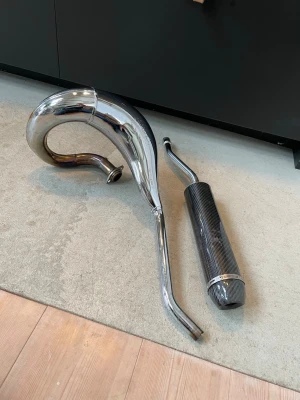 Turbokit rör - Säljer ett komplett avgassystem med böjd kromad expansionskammare och ljuddämpare i kolfiber. Passar till cross eller moped. Snygg design med blanka detaljer och sportig look. Perfekt för dig som vill uppgradera ljud och prestanda.