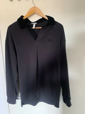 Svart henley-skjorta från H&M - Svart henley-skjorta från H&M med relaxed fit. Skjortan har lång ärm, knappar vid halsen och en klassisk krage i manchester. Perfekt för en chill och stilren look.