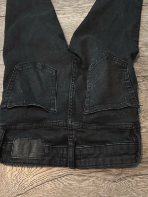 Svarta skinny jeans från 157 - Säljer ett par svarta skinny jeans från 157 med raka bakfickor och klassisk passform. Jeansen har en enkel design utan slitningar och är tillverkade i ett stretchigt material som sitter tajt längs benen. Perfekta för en stilren och avslappnad look.