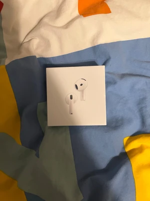 Apple AirPods 4th generation - Säljer ett par Apple AirPods 4th generation i originalförpackning. De är vita, har en stilren och modern design med rundade former och är tillverkade i plast. Perfekta för trådlös musiklyssning och samtal.