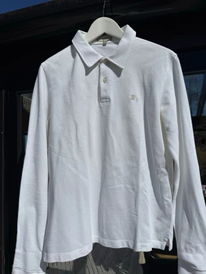 Burberry piké  - Klassisk vit långärmad pikétröja från Burberry med broderad logga på bröstet. Tröjan har krage, två knappar och är tillverkad i ett mjukt bomullsmaterial, synligt klassiskt mönster i krage. Perfekt för en clean och stilren look. Använt fåtal gånger, perfekt skick. Säljer för ett lågt pris då jag är osäker om den är riktig.
