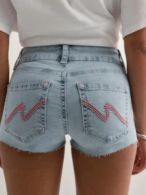Ljusblå low waist jeansshorts - Snygga ljusblå jeansshorts med låg midja och råa kanter. Bakfickorna har ett vågigt broderi i rosa och vitt som ger en unik touch. Perfekta för varma dagar och enkel att matcha med olika toppar.