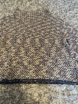 Beige och svart grovstickad tröja - Säljer en grovstickad tröja i beige och svart med hög hals. Tröjan har en chunky känsla och är perfekt för kalla dagar. Materialet ser ut att vara ullblandning och modellen är rak med långa ärmar.