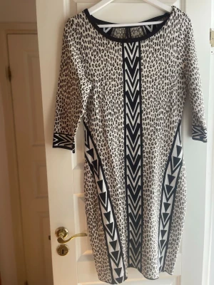 Leopardmönstrad klänning Marc Cain - Snygg leopardmönstrad klänning från Marc Cain med svarta och vita grafiska detaljer framtill och på ärmarna. Klänningen har trekvartsärm och är i en mjuk, stretchig kvalitet som formar sig efter kroppen. Perfekt för dig som vill sticka ut med ett coolt mönster.