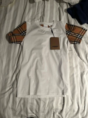 Vit Burberry t-shirt med rutiga ärmar - Burberry t-shirt den är storlek M men den är väldigt kort, passar S mellan 170-180 cm