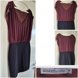 Tvåfärgad klänning från Soaked in Luxury - Snygg klänning från Soaked in Luxury med vinröd överdel och svart kjoldel. Djup v-ringning och korta ärmar ger en modern look. Klänningen har en markerad midja och rak kjol, perfekt för dig som gillar stilrena plagg.