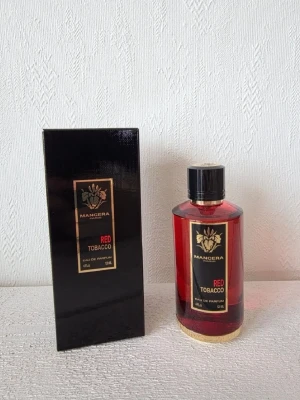 Mancera Red Tobacco Eau de Parfum - Mancera Red Tobacco Eau de Parfum i en elegant röd glasflaska med svart och guld detaljer. Flaskan har en rund form och medföljande svart kartong med guldtext. Doften är intensiv och lyxig, perfekt för dig som gillar kraftfulla parfymer.