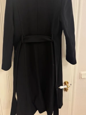 Mango kappa - Säljer en svart MNG lång rock med knytskärp i midjan och breda slag. Materialet är en ullblandning.