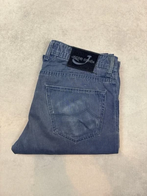 Blå jeans från Jacob Cohen - Snygga blå jeans från Jacob Cohen med klassisk femficksdesign och raka ben. Jeansen har en diskret tvättad look och patch med logga bak i midjan. Perfekta för dig som gillar stilrena och tidlösa jeans i mjukt denimtyg.
