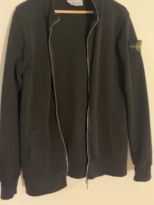 Svart hoodie från Stone Island - Svart hoodie från Stone Island med dragkedja framtill och två fickor. Klassisk patch med logga på vänster ärm. Tillverkad i bomullsmaterial. Perfekt för en clean och stilren look. Liten i storlek så passar S. Pris kan diskuteras vid snabbt köp🙂