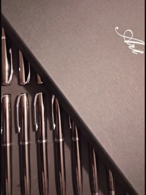 Set med 20 silvriga bläckpennor - Säljer ett exklusivt set med 20 silvriga bläckpennor i metall, levereras i en snygg svart presentask med texten 'Art' på locket. Pennorna har elegant design med metallisk finish och silverdetaljer. Perfekt för skrivbordet eller som present till någon som gillar att skriva.