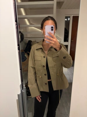 Grön jacka slutsåld från Hm  - Säljer en superfin och helt oanvänd jacka från H&M i en snygg khakigrön/beige ton. Jackan har en lätt figursydd passform med guld detaljer. HELT SLUTSÅLD PÅ HEMSIDAN
