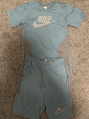 Nike shorts set - Snygga blå Nike set med grå paneler på sidorna . Setet har en sportig look och är perfekta för träning eller chill. Nike-logga framtill i vitt. 