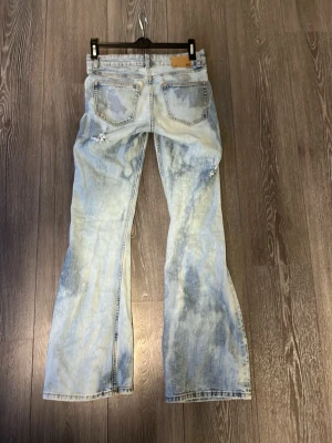 Ljusblå slitna bootcut jeans - Snygga ljusblå bootcut jeans med slitningar och hål på benen. Jeansen har klassisk och en tvättad look som ger en cool vintagekänsla. Perfekta för dig som gillar en avslappnad och trendig stil.