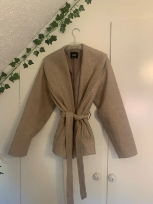 Beige kappa från ONLY med knytskärp - Säljer en snygg kappa från only med knyt i midjan. Kappan är både bekväm och fin. Dessutom passar den för alla tillfällen. Detaljien i midjan gör att man kan anpassa storleken i midjan och som gör den unik🩷Prisst går att diskutera