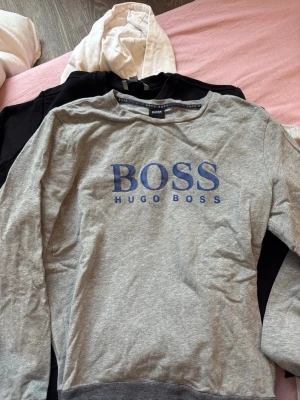 Grå sweatshirt från Hugo Boss - Grå långärmad sweatshirt från Hugo Boss med blått BOSS-tryck på bröstet. Passar s/m