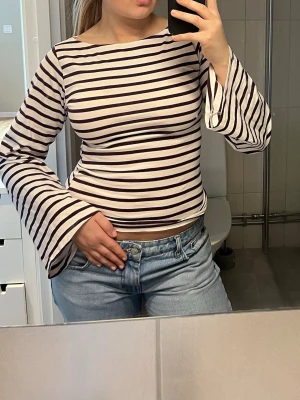 Randig långärmad topp med utsvängda ärmar - Snygg långärmad topp med svartvita ränder och utsvängda ärmar. Toppen har en vid halsringning och är gjord i mjuk bomull🌟