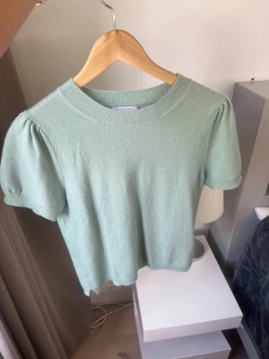Ljusgrön kashmir topp med puffärm - Supersöt ljusgrön kashmir topp med korta puffärmar och rund halsringning. Mjuk och skön kvalitet som känns lyxig och passar perfekt till jeans eller kjol. Enkel men ändå trendig design som ger en fräsch look.