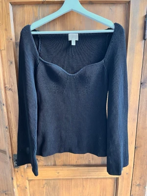 Svart ribbad topp med sweetheart-ringning - Snygg svart långärmad topp med ribbad struktur och markerad sweetheart-ringning. Figurnära passform och stretchigt material som sitter bekvämt. Perfekt att styla med jeans eller kjol för en trendig look.