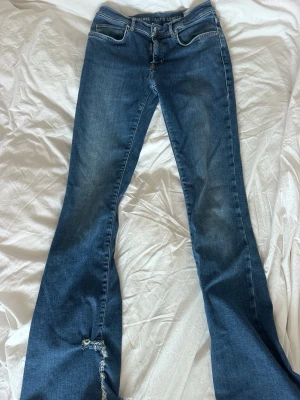 Blå low flare jeans med slitning - Snygga blå jeans med low flare-modell och låg midja. Längd 33 och storlek S. Jeansen har en klassisk femficksdesign. Perfekta för dig som gillar en trendig och avslappnad stil.
