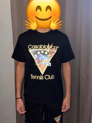 Svart Casablanca Tennis Club Set - Cool svart Set från Casablanca med stort färgglatt tryck på bröstet där det står 'Casablanca Tennis Club' och ett grafiskt motiv med pyramid, växter och månar. Klassisk passform och rund hals. Perfekt för dig som gillar streetwear och unika prints.