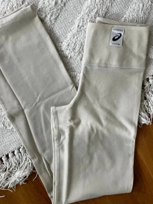 Beige leggings från Asics - Snygga bootcut leggings från Asics med hög midja. Tillverkade i ett stretchigt material som sitter skönt och följer kroppen. 