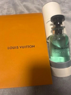 Louis Vuitton Imagination parfym - Lyxig parfym från Louis Vuitton med namnet Imagination. Flaskan är genomskinlig med ljusblå vätska och har en elegant svart kork. Kommer i originalförpackning med en snygg orange ask och vit cylinderformad kartong. Perfekt för dig som gillar exklusiva dofter.